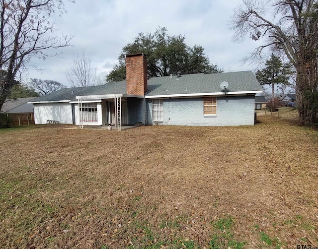 rear view of property with brick siding, a yard, and a chimney