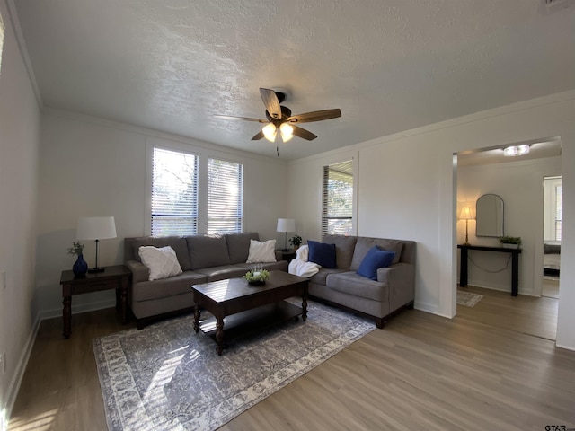 living room featuring a ceiling fan, baseboards, ornamental molding, a textured ceiling, and light wood-type flooring