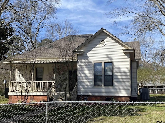 back of property with central air condition unit, a lawn, roof with shingles, and fence