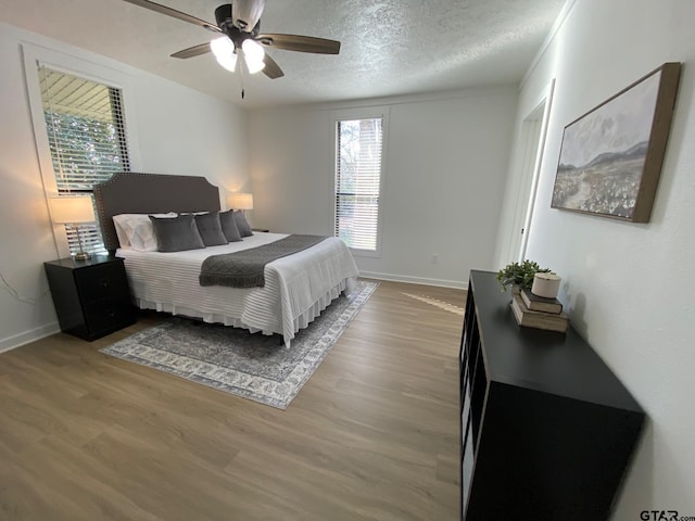 bedroom with ceiling fan, baseboards, a textured ceiling, and wood finished floors