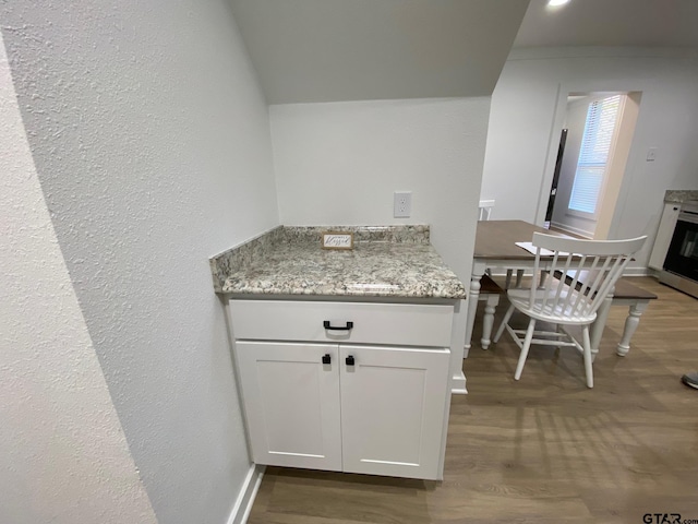 kitchen featuring white cabinets, light stone countertops, lofted ceiling, and wood finished floors