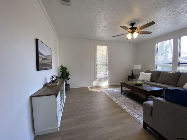 living room featuring visible vents, a textured ceiling, wood finished floors, baseboards, and ceiling fan