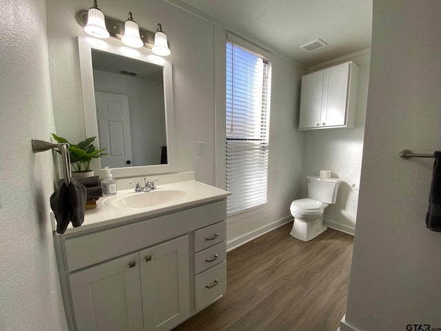 half bath with visible vents, toilet, wood finished floors, baseboards, and vanity