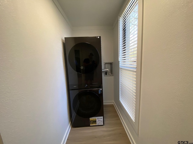 clothes washing area featuring stacked washer and clothes dryer, ornamental molding, wood finished floors, baseboards, and laundry area