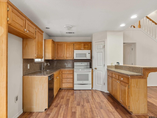 kitchen with sink, white appliances, light hardwood / wood-style flooring, dark stone countertops, and decorative backsplash