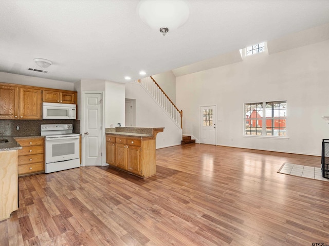 kitchen with backsplash, a high ceiling, kitchen peninsula, white appliances, and light hardwood / wood-style flooring