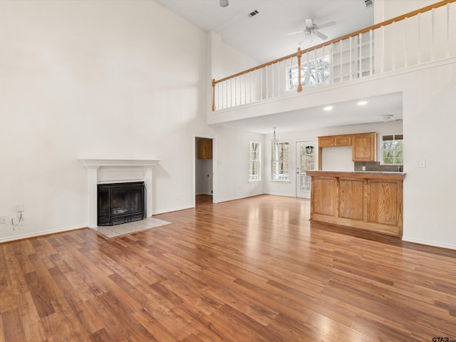 unfurnished living room with ceiling fan, a high ceiling, and light wood-type flooring