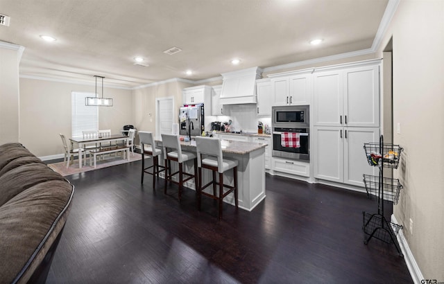 kitchen with white cabinetry, appliances with stainless steel finishes, custom range hood, a kitchen bar, and an island with sink