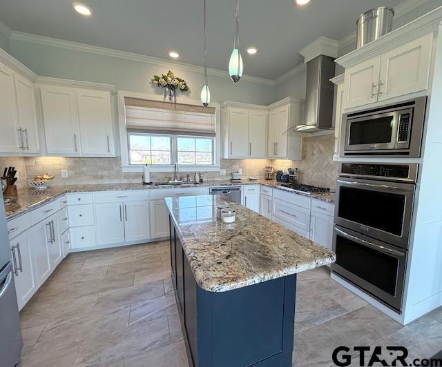 kitchen with a kitchen island, white cabinets, wall chimney range hood, appliances with stainless steel finishes, and tasteful backsplash