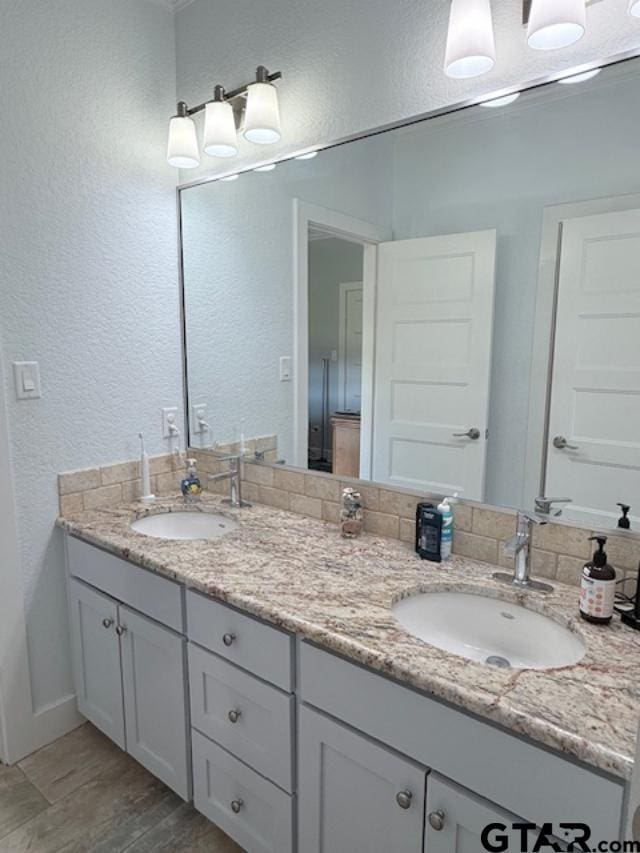 full bath with a textured wall, wood finished floors, a sink, and double vanity