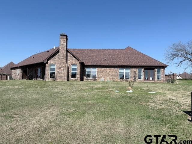 back of property with a chimney, a lawn, and brick siding