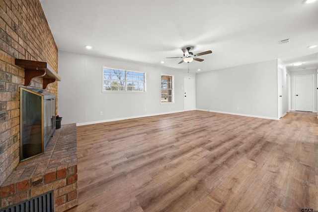 unfurnished living room with a brick fireplace, hardwood / wood-style flooring, and ceiling fan