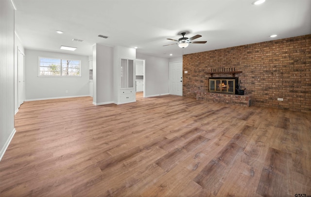 unfurnished living room featuring ceiling fan, brick wall, light hardwood / wood-style floors, and a brick fireplace