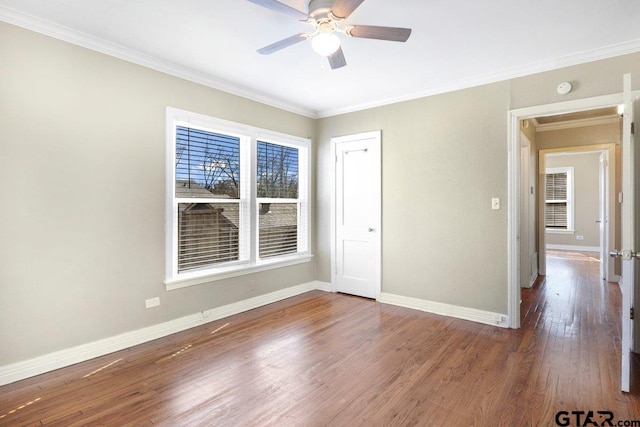 empty room with a ceiling fan, dark wood-style flooring, crown molding, and baseboards