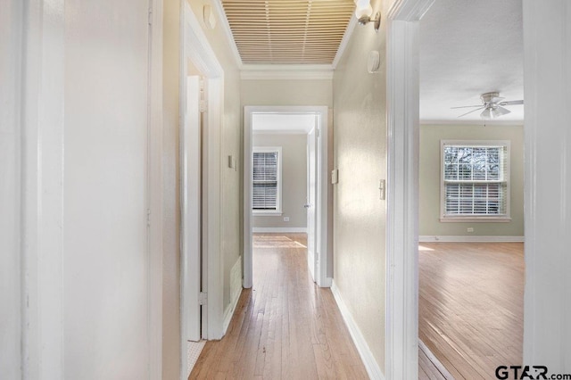 hallway featuring baseboards, visible vents, light wood-style flooring, and crown molding