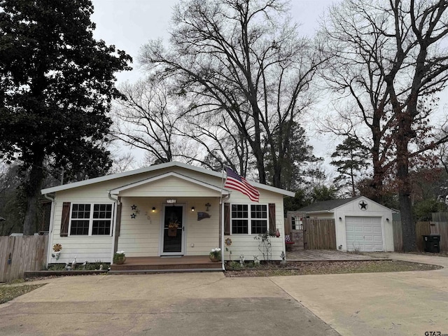 bungalow-style home featuring covered porch, an outdoor structure, fence, a detached garage, and driveway