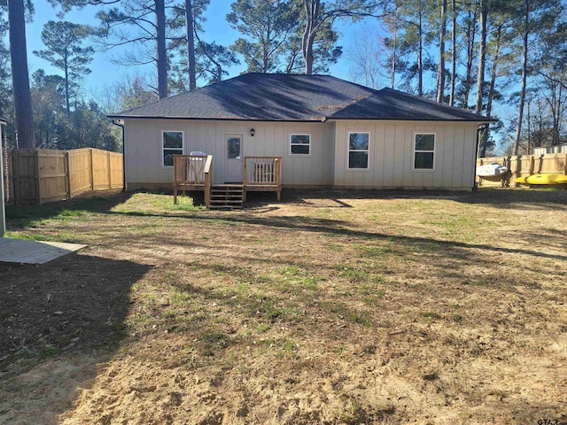 back of property with a fenced backyard, a deck, a lawn, and roof with shingles