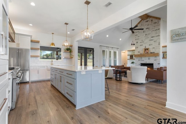 kitchen with a center island, a stone fireplace, premium appliances, decorative light fixtures, and light hardwood / wood-style floors