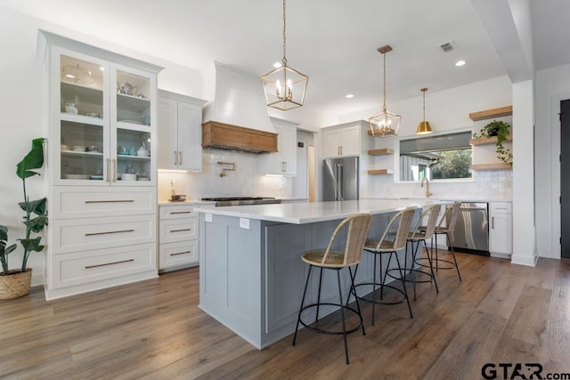 kitchen with appliances with stainless steel finishes, custom exhaust hood, a spacious island, white cabinets, and hanging light fixtures