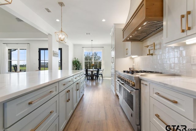 kitchen featuring white cabinetry, range with two ovens, custom range hood, and a healthy amount of sunlight