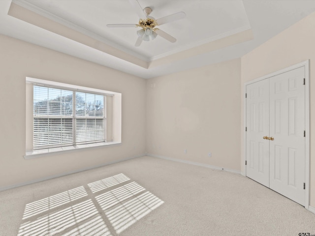 unfurnished bedroom featuring crown molding, light carpet, a closet, and a tray ceiling