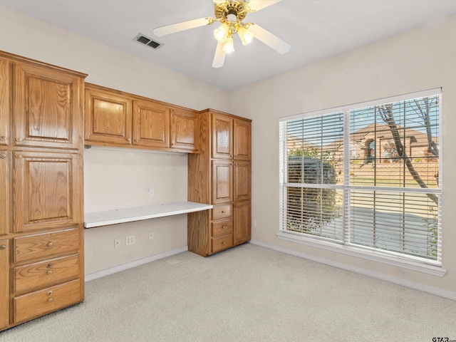 unfurnished office with built in desk, light colored carpet, and ceiling fan