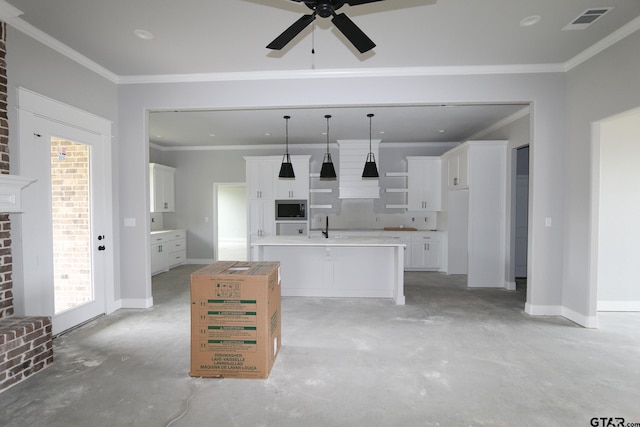 kitchen with a center island with sink, white cabinets, stainless steel microwave, ornamental molding, and decorative light fixtures