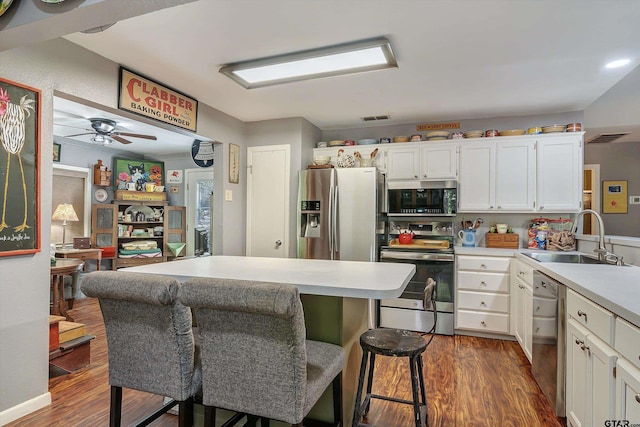 kitchen with a kitchen bar, stainless steel appliances, dark hardwood / wood-style flooring, sink, and white cabinetry