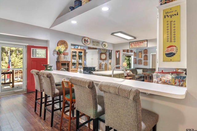 kitchen with dark wood-type flooring, kitchen peninsula, vaulted ceiling, and a kitchen breakfast bar