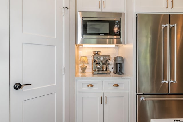 bar with tasteful backsplash, white cabinetry, and appliances with stainless steel finishes