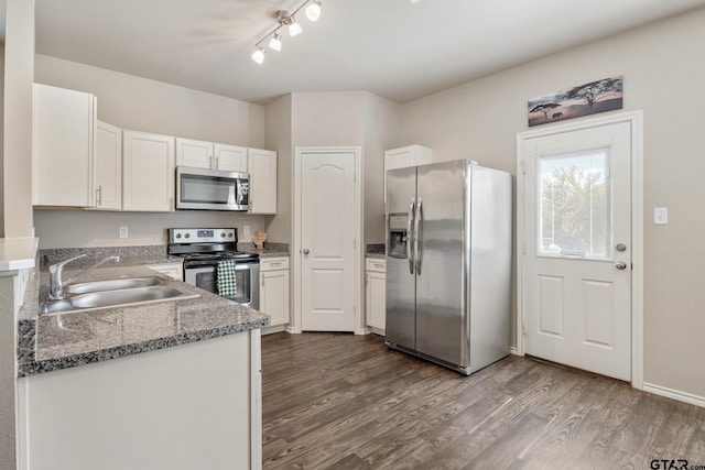 kitchen with stainless steel appliances, hardwood / wood-style flooring, sink, white cabinetry, and dark stone countertops