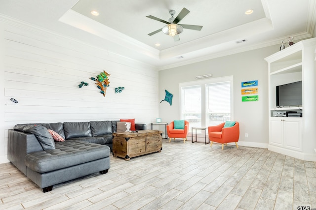 living room with ornamental molding, light hardwood / wood-style floors, a raised ceiling, and ceiling fan