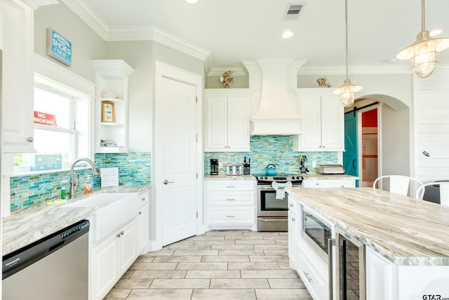 kitchen featuring appliances with stainless steel finishes, white cabinets, custom exhaust hood, hanging light fixtures, and light stone counters