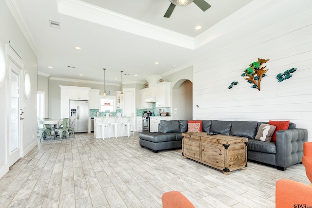 living room with crown molding, light hardwood / wood-style floors, a raised ceiling, and ceiling fan