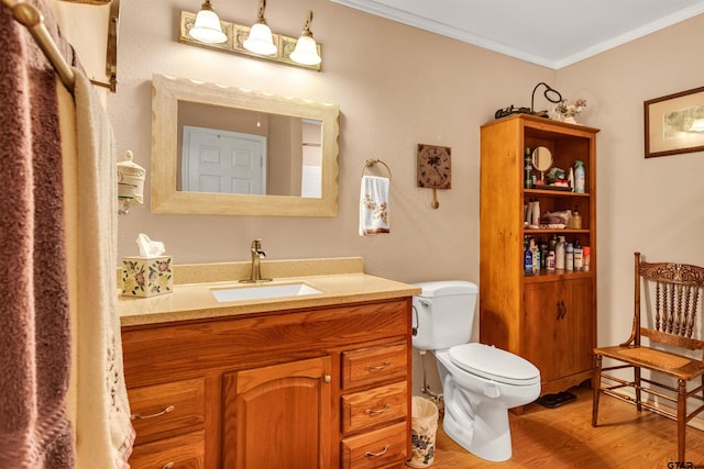 bathroom with vanity, toilet, wood finished floors, and crown molding