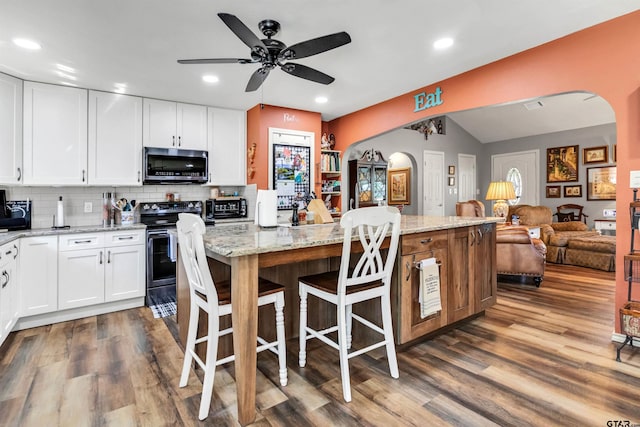 kitchen with a center island, light stone countertops, arched walkways, stainless steel appliances, and dark wood-style flooring