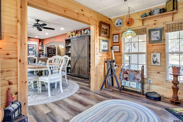 dining space with wood finished floors, arched walkways, ceiling fan, wood walls, and a barn door