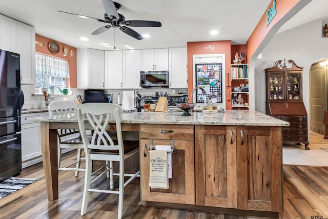 kitchen with a sink, stainless steel microwave, backsplash, white cabinetry, and arched walkways