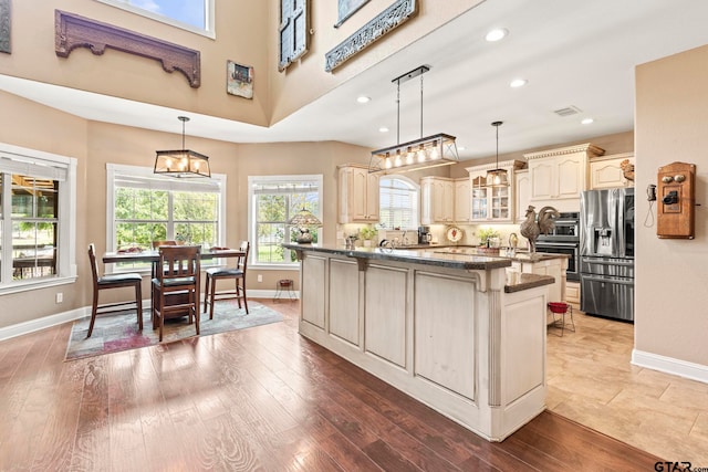 kitchen with pendant lighting, hardwood / wood-style flooring, stainless steel fridge, cream cabinets, and a kitchen island