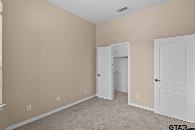 unfurnished bedroom featuring a walk in closet and light carpet