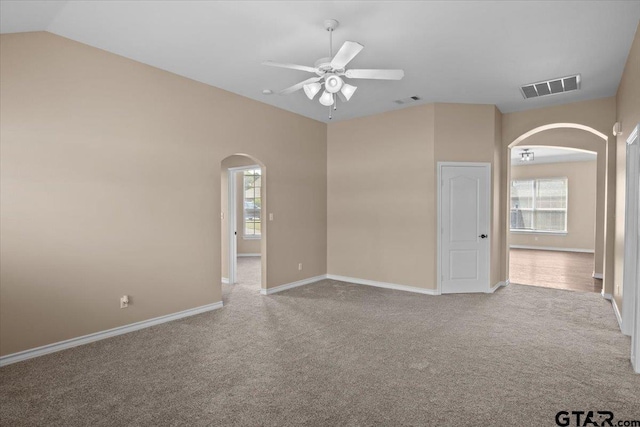 empty room featuring light colored carpet, vaulted ceiling, ceiling fan, and a healthy amount of sunlight