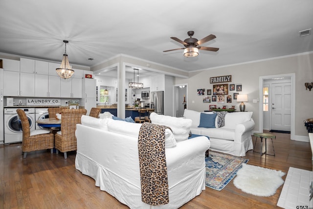 living area with ornamental molding, washer and dryer, visible vents, ceiling fan with notable chandelier, and wood finished floors