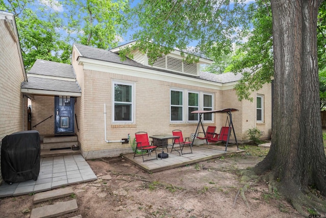 back of house featuring brick siding and roof with shingles