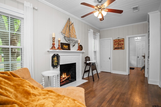 living room with wood finished floors, a fireplace, visible vents, ceiling fan, and ornamental molding