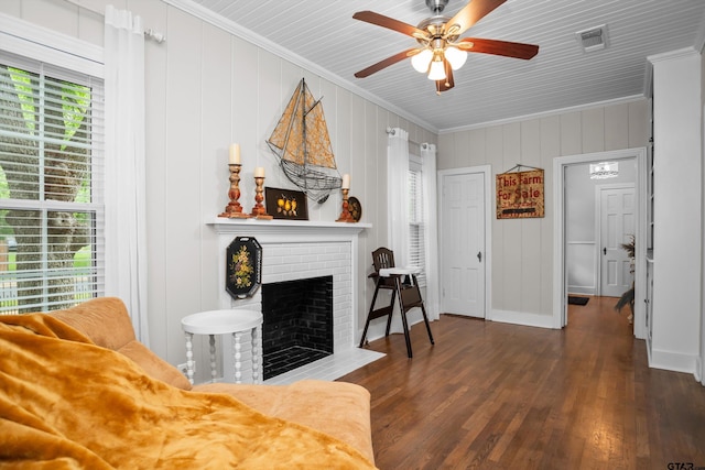 living room with a ceiling fan, visible vents, a brick fireplace, crown molding, and wood finished floors