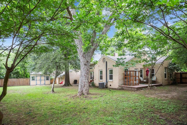 view of yard featuring a fenced backyard, an outdoor structure, central air condition unit, a wooden deck, and a storage shed