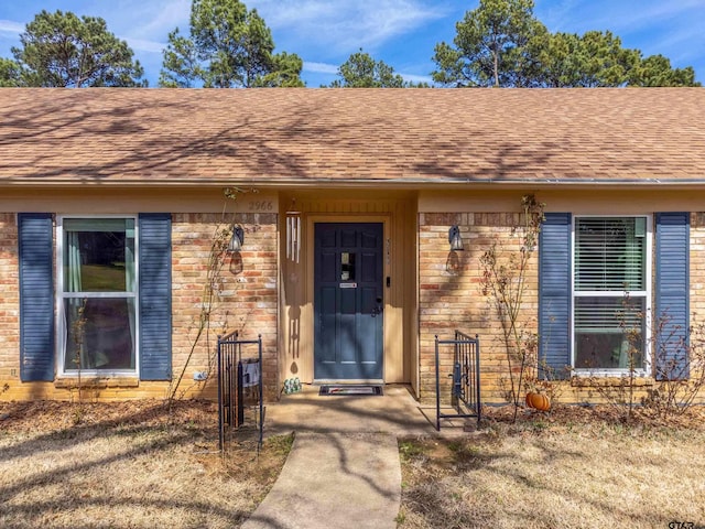 property entrance featuring a shingled roof and brick siding