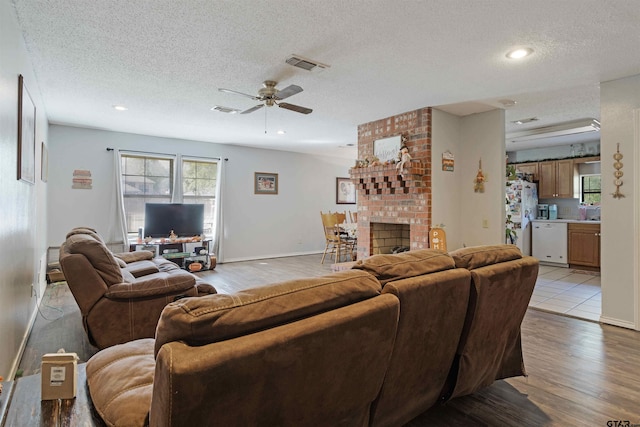 living room featuring a brick fireplace, light hardwood / wood-style floors, a textured ceiling, and ceiling fan