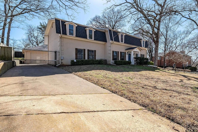 view of front facade featuring mansard roof, brick siding, fence, roof with shingles, and a gate