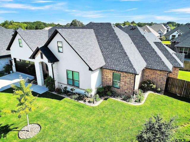 view of front of home with brick siding, a shingled roof, a front yard, fence, and a garage